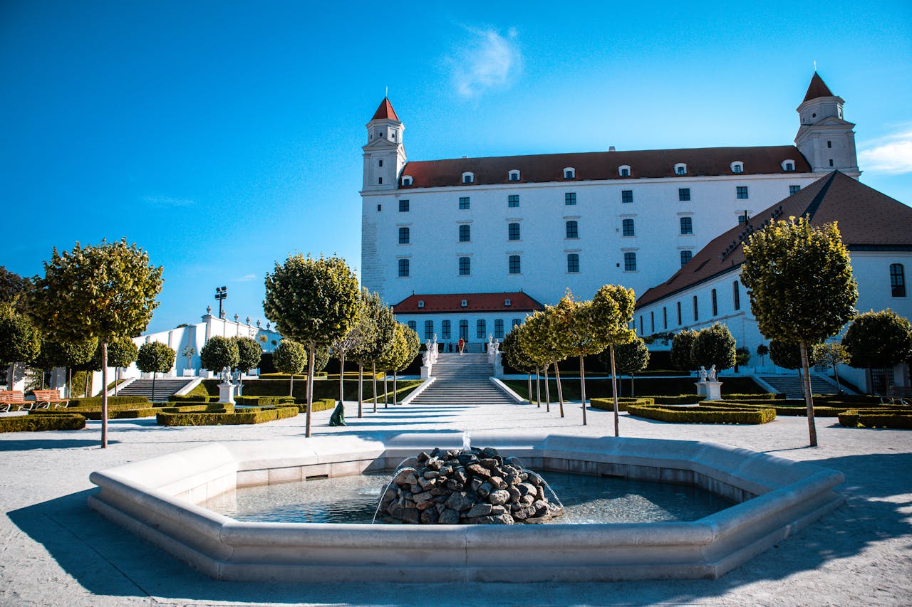 Elegant baroque garden featuring a historic castle and central fountain under a clear blue sky.